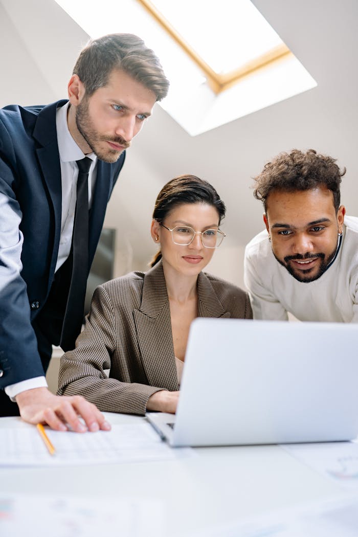 Three professionals collaborating around a laptop in a modern office setting.